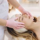 Woman receiving relaxing spa facial skincare treatment from esthetician, headband and pink gloves