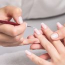 Close-up of a nail technician applying French manicure white tips to a woman's well-groomed nails